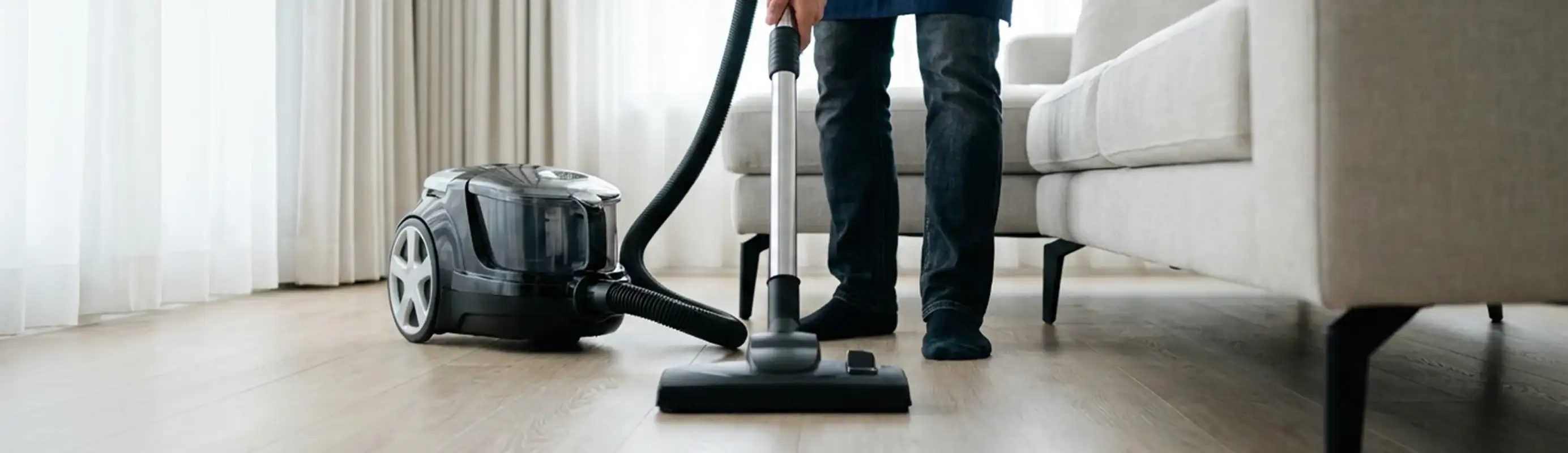 Professional house cleaner vacuuming a living room floor with a canister vacuum cleaner, San Francisco, CA.