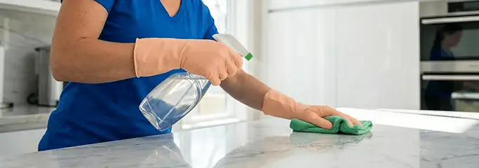 Maid service worker spraying and wiping a kitchen countertop with a microfiber cloth for sanitizing, San Francisco, CA.
