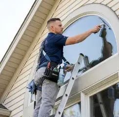 Professional window cleaner on a ladder using a squeegee to clean an exterior arched window, San Francisco, CA.