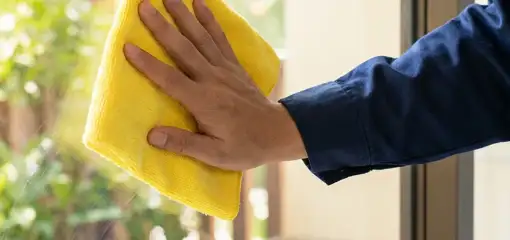 House cleaner wiping a glass window with a yellow microfiber cloth for streak-free cleaning, San Francisco, CA.